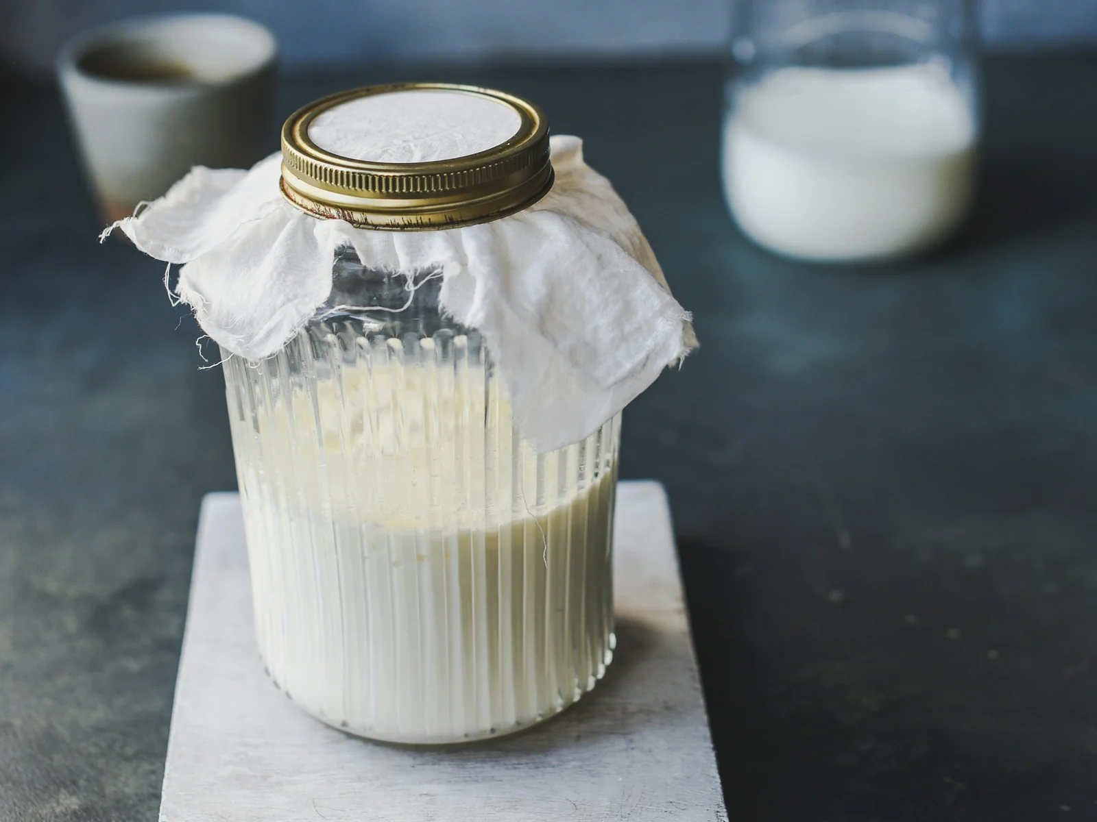 A glass jar of cultured milk covered with a cloth, beside a small bottle of milk