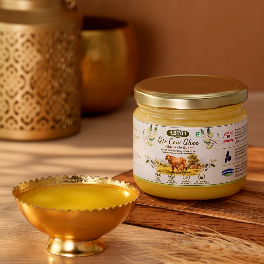 A 250 ml jar of AB704 beside a brass bowl of warm ghee, lit by low evening light