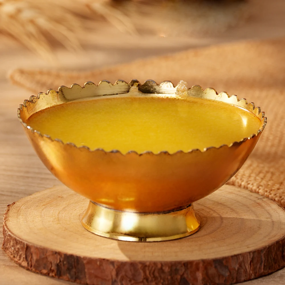 Molten ghee in a scalloped brass bowl resting on a wooden slice